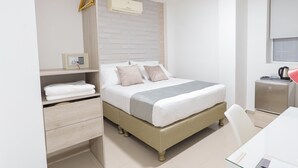 Un dormitorio con cama, mesita de noche, armario, escritorio y una pequeña kitchenette.