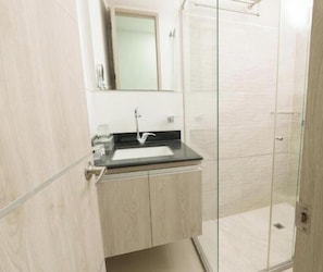 Un baño con cabina de ducha de vidrio, lavamanos con espejo y tocador de madera.