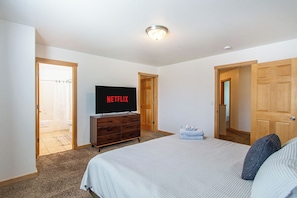 A bedroom with a bed, a TV on a dresser, and wooden doors.