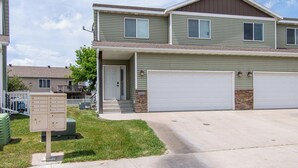 A two-story residential building with a garage, a mailbox, and a small front yard. - 3BR | 7 minutes to Sanford, Fenced Yard, Games (Fargo)