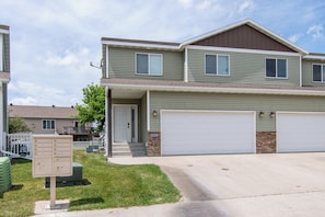 A two-story residential building with a garage, a mailbox, and a small front yard.