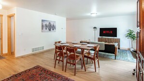 A modern living room with a dining area, a flat-screen TV, and a large window. - 3BR | 7 minutes to Sanford, Fenced Yard, Games (Fargo)