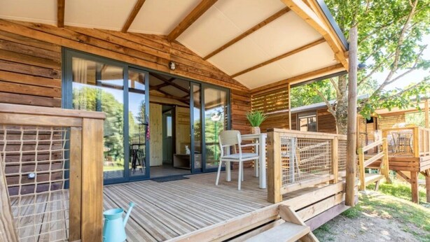 A wooden deck with a glass door leading to a room, a chair, a small table, and a plant. - Chalet 3 étoiles - ccbgcfc (Saint-Bonnet-près-Orcival)