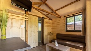 A wooden interior with a sofa, a small table, a TV, and a window. - Chalet 3 étoiles - ccbgcfc (Saint-Bonnet-près-Orcival)