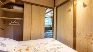 A wooden room with a bed, a hanging light fixture, and a window. - Chalet 3 étoiles - ccbgcfc (Saint-Bonnet-près-Orcival)