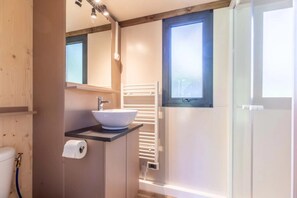 Un baño moderno con un lavamanos blanco, un espejo, un perchero para toallas y una ventana.