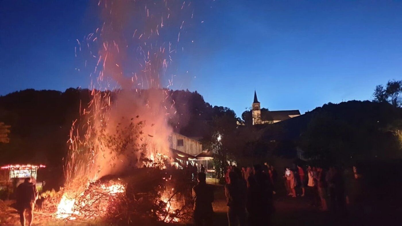 Nachtszene mit Feuer, einem Gebäude mit Turm und einer Menschenmenge.
