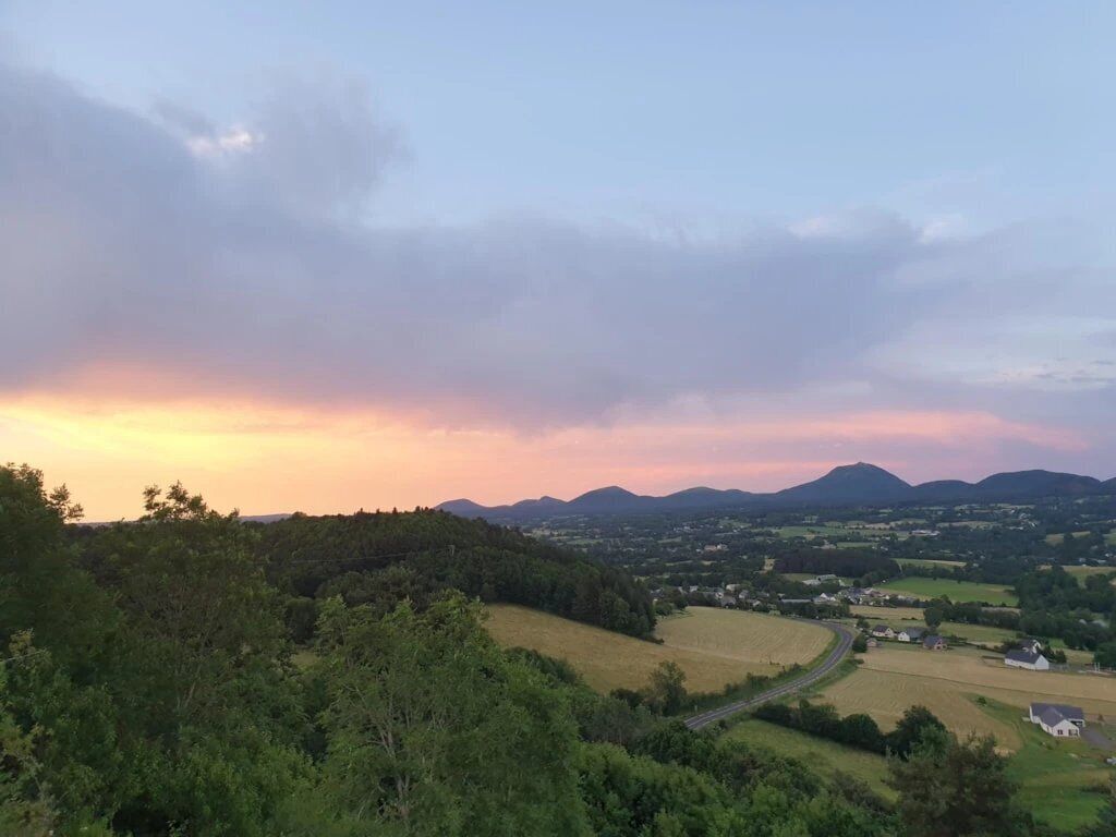 A rural landscape with a winding road, a forested area, and distant hills.