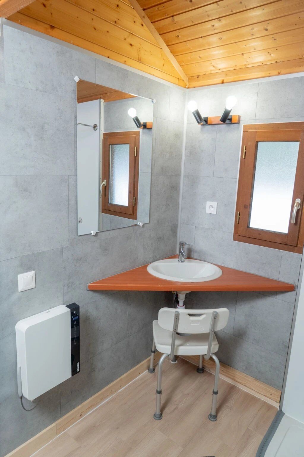 Een badkamer met een houten wastafelmeubel, een spiegel, een wastafel, een stoel en een radiator.