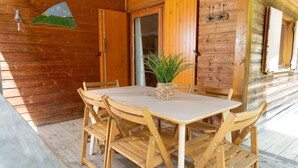 Eine Holzjagd- oder Berghütte mit Esstisch, Stühlen, einem Blumentopf und einer Tür mit Klingel.