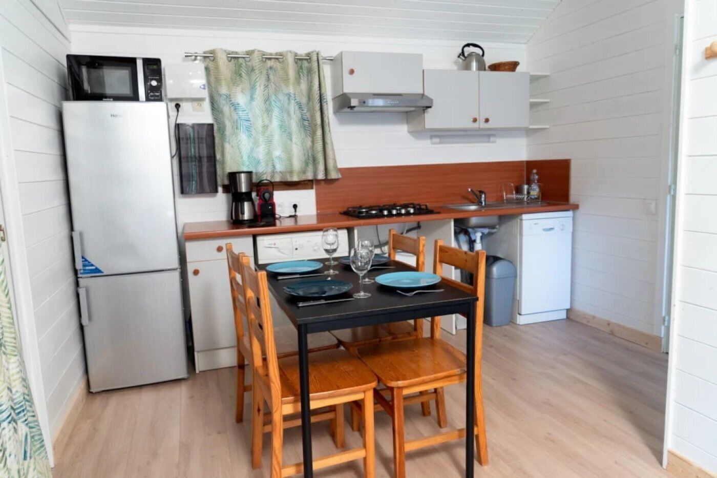 A compact kitchen with a refrigerator, microwave, stove, and a dining table set with chairs.