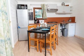 Uma cozinha compacta com geladeira, fogão, micro-ondas e uma pia pequena. Há uma mesa de jantar com cadeiras e uma janela com cortinas.