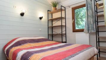 Een kamer met een bed, wandplanken, een raam met gordijnen en een plant.