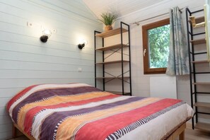 Une pièce comprenant un lit, des étagères fixées au mur, une fenêtre avec des rideaux et une plante.