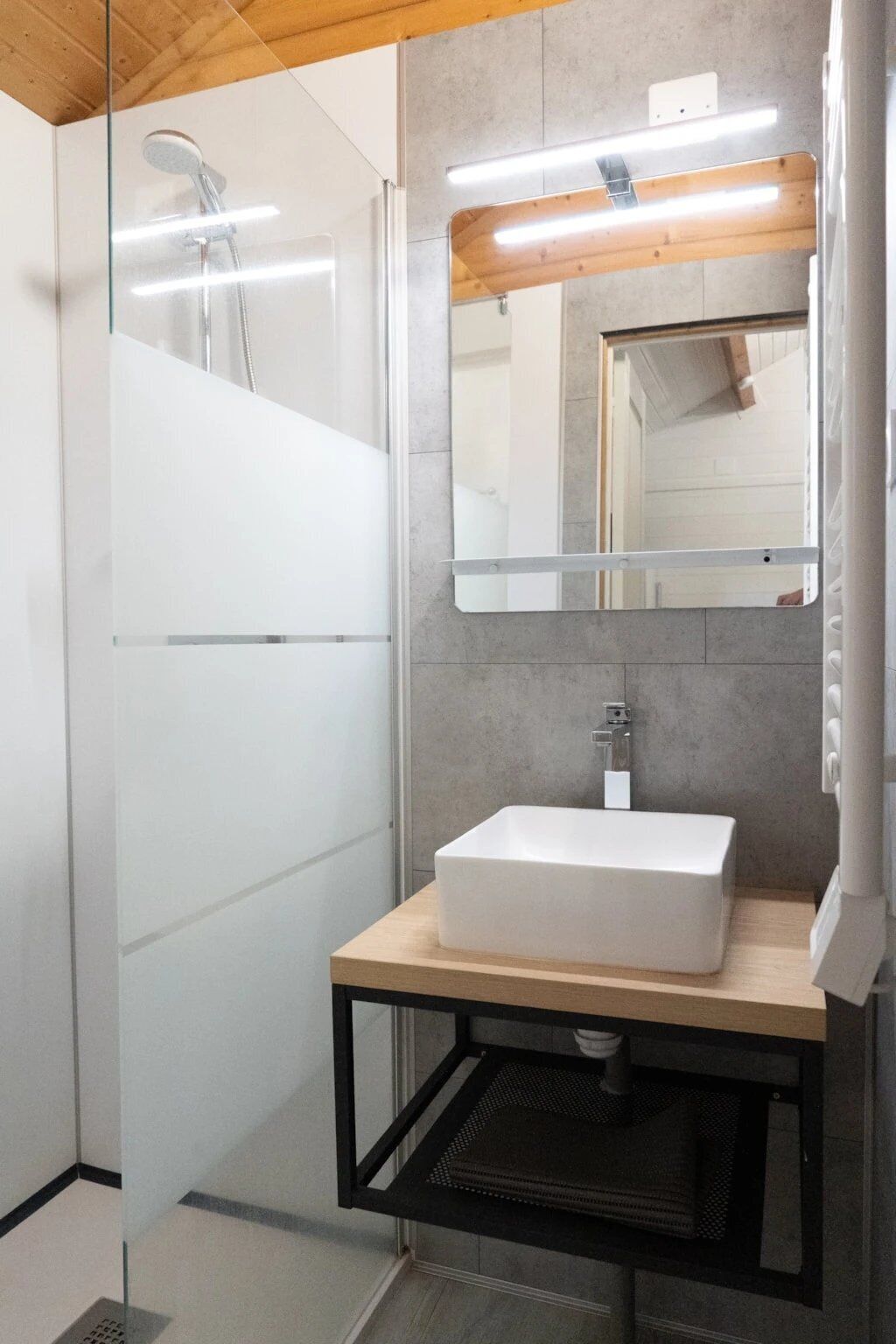 Een moderne badkamer met een douchecabine van glas, een wit wastafelmeubel en een spiegel erboven.
