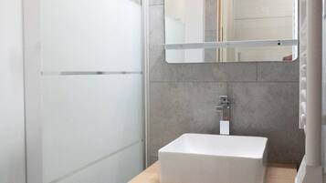 Een moderne badkamer met een douchecabine van glas, een wit wastafelmeubel en een spiegel erboven.