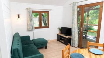 Een gezellige kamer met een groene bank, een televisie op een houten standaard en een eettafel met stoelen.
