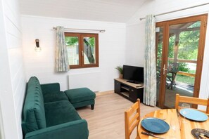 Une pièce chaleureuse avec un canapé vert, un téléviseur posé sur un meuble en bois et une table à manger avec des chaises.