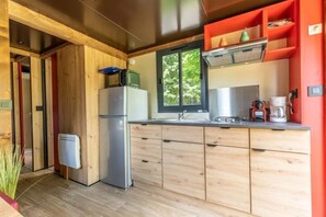 A modern kitchen with wooden cabinets, a stainless steel refrigerator, a window with a view, and a red accent wall. - Camping 3 étoiles - ccbgcfh (Saint-Bonnet-près-Orcival)
