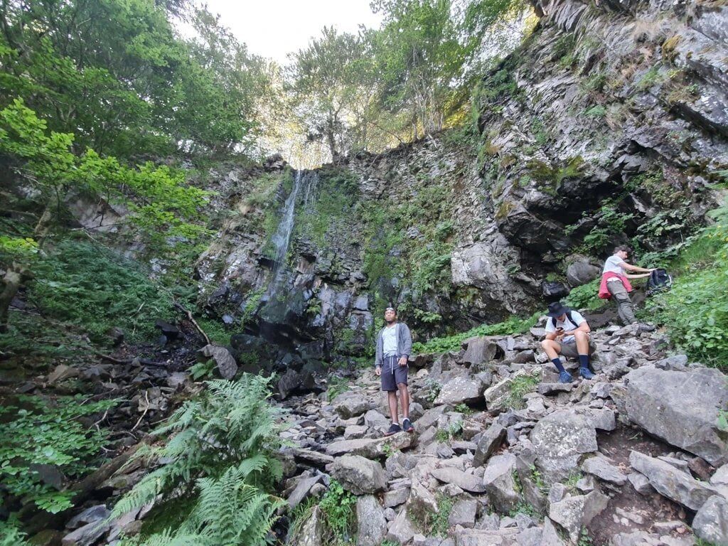 Uma área rochosa ao ar livre com uma cascata, rodeada por vegetação densa.