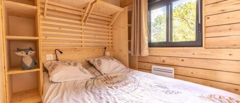 A wooden cabin bedroom with a bunk bed, a shelf with a stuffed toy, and a window with curtains.