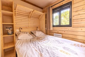 Et soveværelse i en træhytte med køjeseng, en hylde med en stuffedyr og et vindue med gardiner.