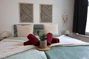 Una cama con una colcha verde, dos almohadas, una manta roja y una planta pequeña sobre una bandeja de madera.