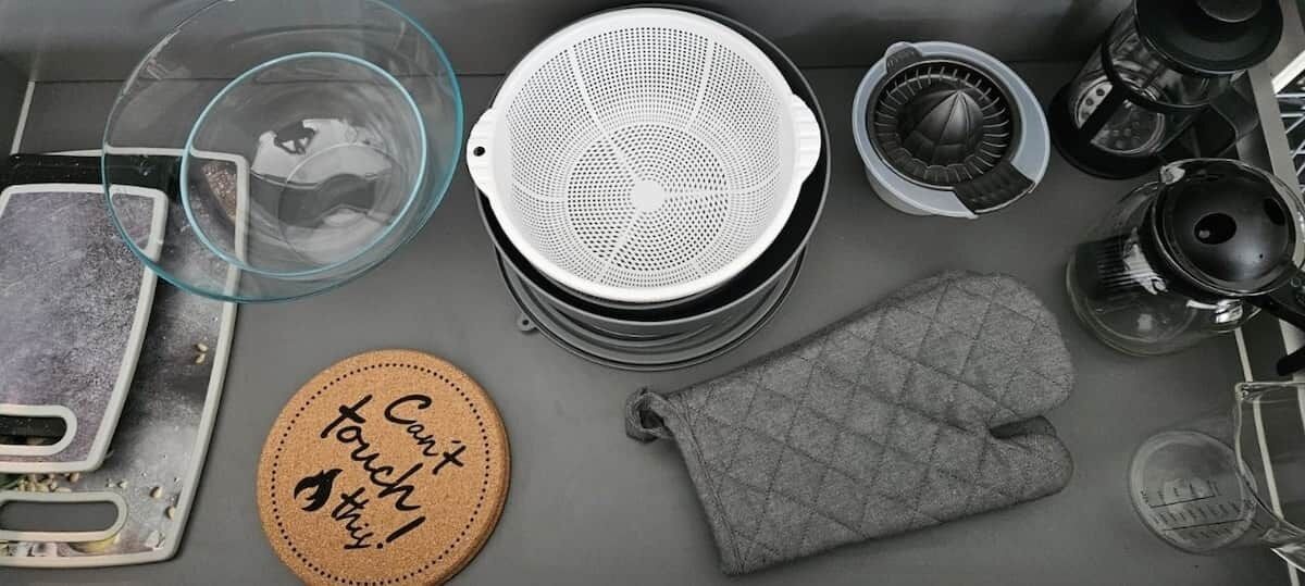 A kitchen with a coffee maker, a kettle, a tea kettle, a glass container, a cloth, and a coaster with text.
