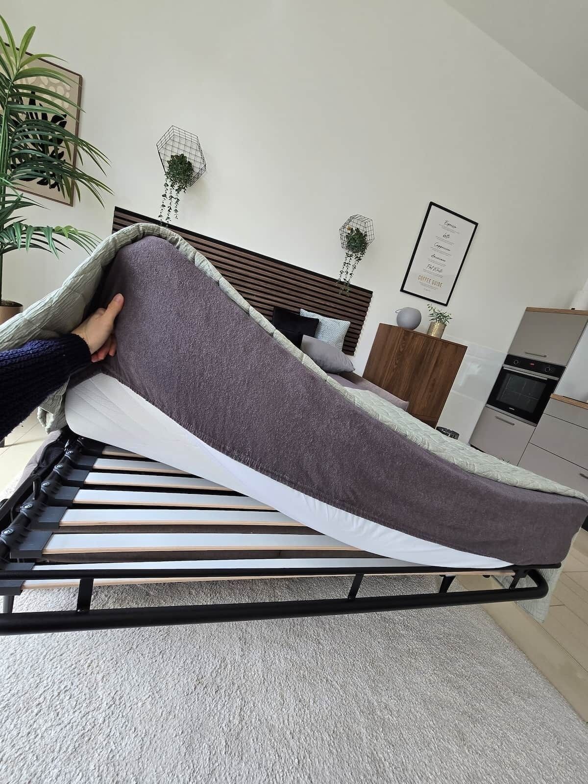 Un lit avec un matelas gris, une tête de lit en bois, un oreiller blanc et une couverture grise.