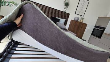 Un lit avec un matelas gris, une tête de lit en bois, un oreiller blanc et une couverture grise.