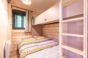 Une chambre dans un chalet en bois, avec un lit superposé, une fenêtre avec des rideaux et une petite table.