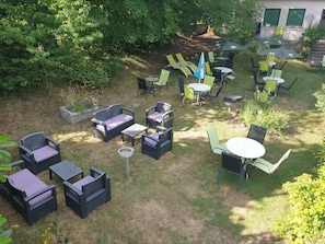 An outdoor seating area with multiple tables and chairs, surrounded by greenery and trees. - Chalet 3 étoiles - ccbgcgb (Saint-Bonnet-près-Orcival)