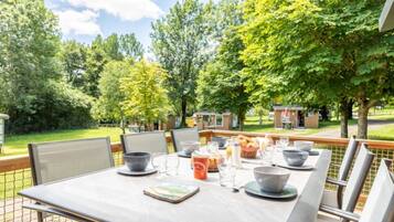 Een terras met een tafel gedekt voor vier personen, omringd door stoelen, met uitzicht op een tuin en een gebouw op de achtergrond.