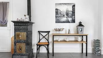 Ein Zimmer mit einem alten Herd, einem Sessel, einem Tisch mit Teekannen und einem Wandbild.
