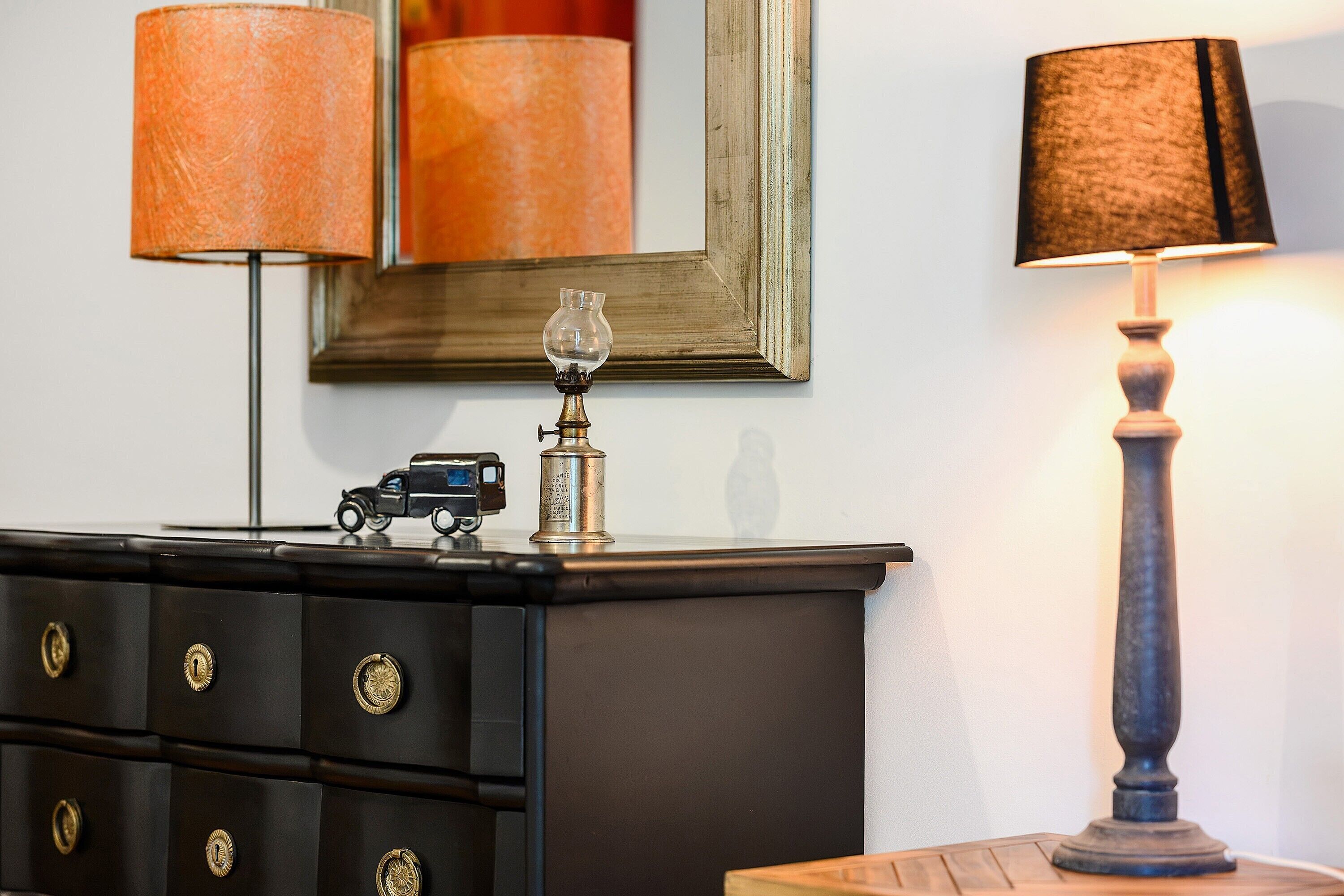 Une commode noire avec des poignées en laiton, une lampe ancienne et une petite voiture jouet posée sur le dessus.