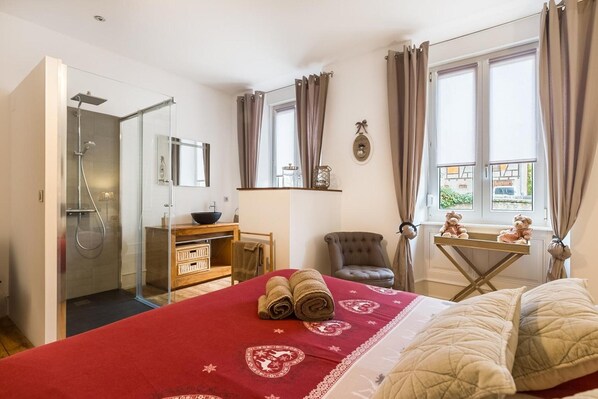 Ein Hotelzimmer mit einem Bett, einer Dusche, einem kleinen Tisch mit einer Schüssel, einem Stuhl und einem Fenster mit Vorhängen.