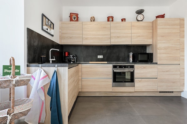 Eine moderne Küche mit Holzschränken, einer schwarzen Arbeitsplatte, einer Kaffeemaschine, einer Mikrowelle und einem eingebauten Backofen.
