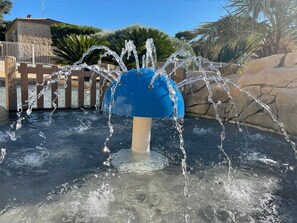 A water fountain with a blue top, surrounded by a stone wall and palm trees.