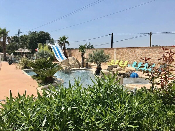 Ein Poolbereich mit Wasserrutsche, Liegestühlen und einer Steinmauer.