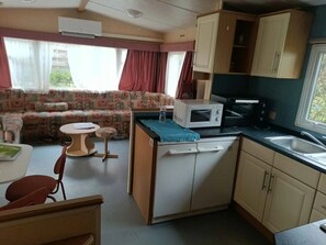 A compact RV kitchen with a microwave, sink, and a small dining area with a sofa and chairs. - Camping 3 étoiles - Piscine  - ccbgbbb (Thiviers)