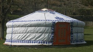 A large, white yurt with blue diamond patterns and a red door, set in a grassy field with trees in the background. - Camping 3 étoiles - ccbgcgd (Prads-Haute-Bléone)
