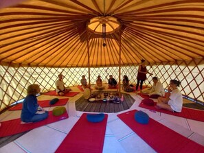A group of people sitting on mats inside a yurt with a central fire pit. - Chalet 3 étoiles - ccbgche (Prads-Haute-Bléone)
