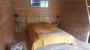 Ett sovrum i en stuga, inrett med en säng, ett litet bord, en lampa och ett fönster.