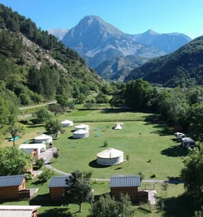 Yurts and wooden cabins in a grassy field with mountains in the background. - Chalet 3 étoiles - ccbgcgf (Prads-Haute-Bléone)