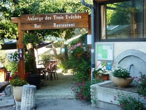 A wooden sign for Auberge des Trois Evêchés Bar Restaurant, outdoor seating, and potted plants. - Chalet 3 étoiles - ccbgcgf (Prads-Haute-Bléone)