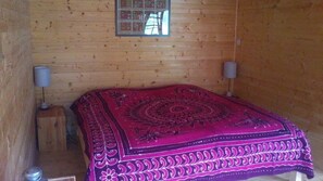 Une pièce de cabane en bois comprenant un lit, deux lampes et une fenêtre.