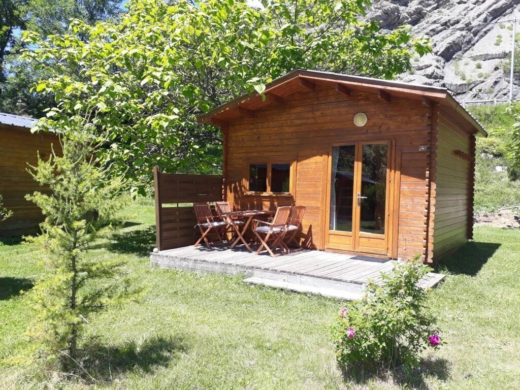 Une cabane en bois avec une terrasse, une table à manger et des chaises.