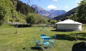 A yurt with a round shape, surrounded by a grassy area with a few chairs and a table.