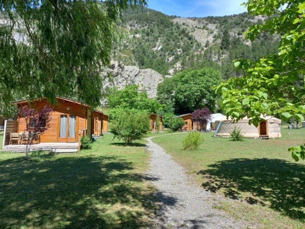 Un chalet rustique avec des cabanes en bois, un chemin de gravier et une chaîne de montagnes en arrière-plan.