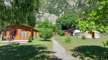 Un chalet rustique avec des cabanes en bois, un chemin de gravier et une chaîne de montagnes en arrière-plan.